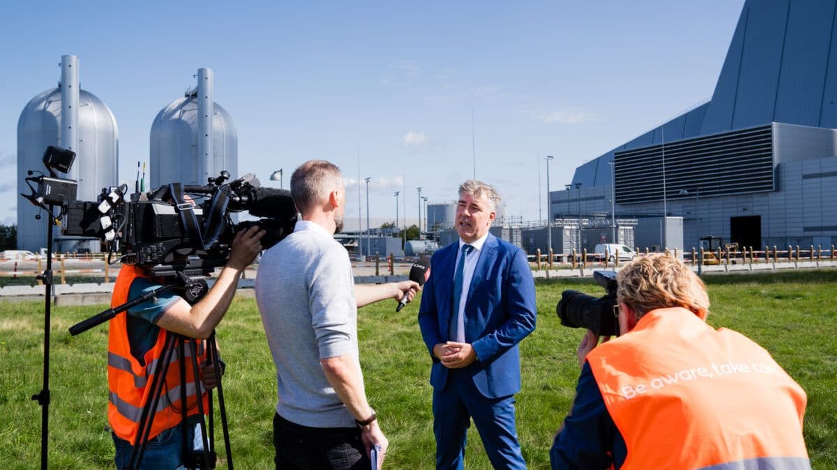 En mann med et kamera foran en fabrikk.