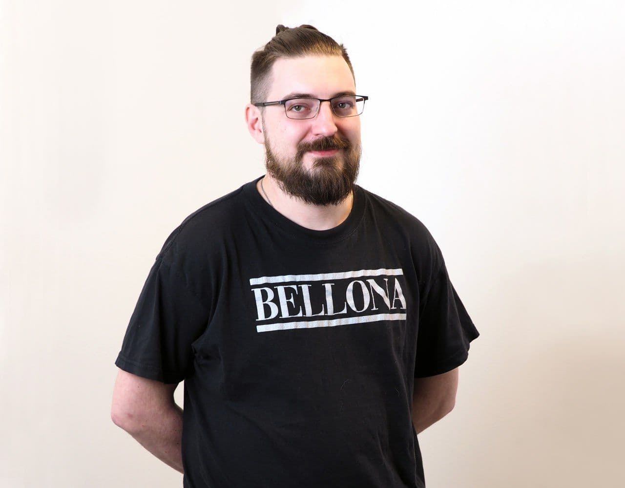 En smilende mann med skjegg, briller og toppknute som har på seg en svart «BELLONA»-t-skjorte.