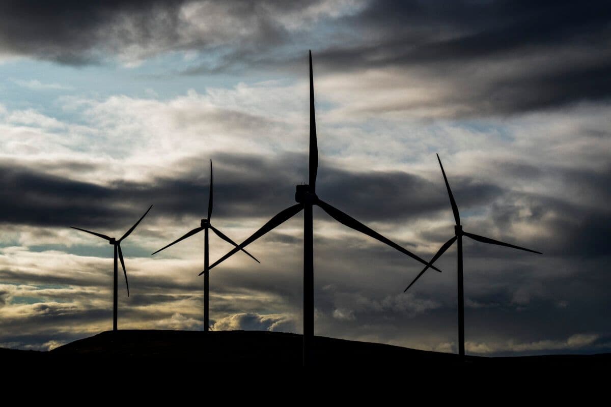 Fire vindturbiner står i et kupert landskap under en overskyet himmel, silhuettert mot det falmende dagslyset.