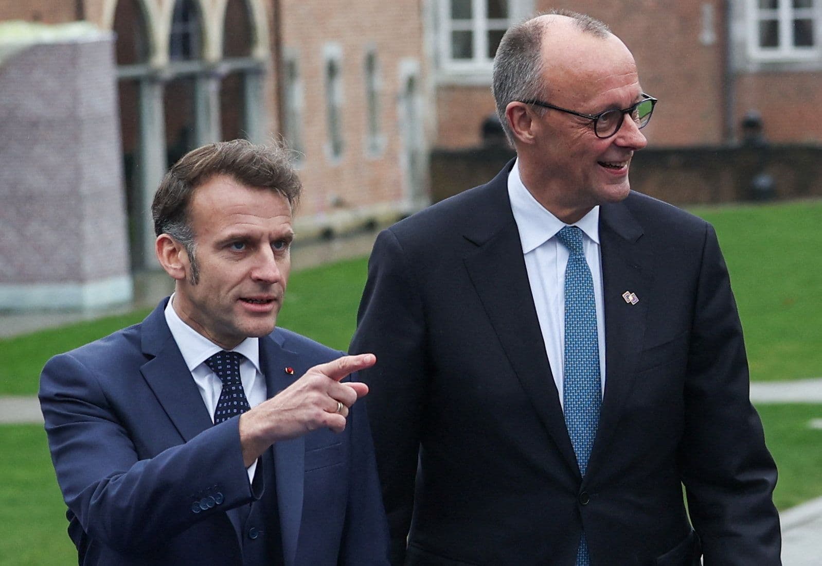 Emmanuel Macron points while walking next to a smiling Friedrich Merz.