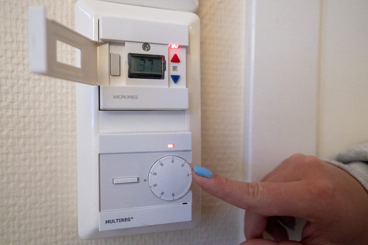 En person justerer en hvit termostat på en vegg ved å vri på en skive med en blåmalt negl.