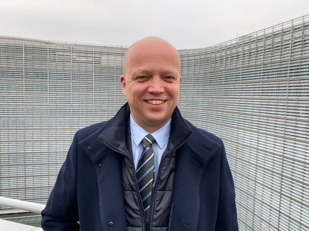 En skallet mann i dress og slips som står foran en bygning.