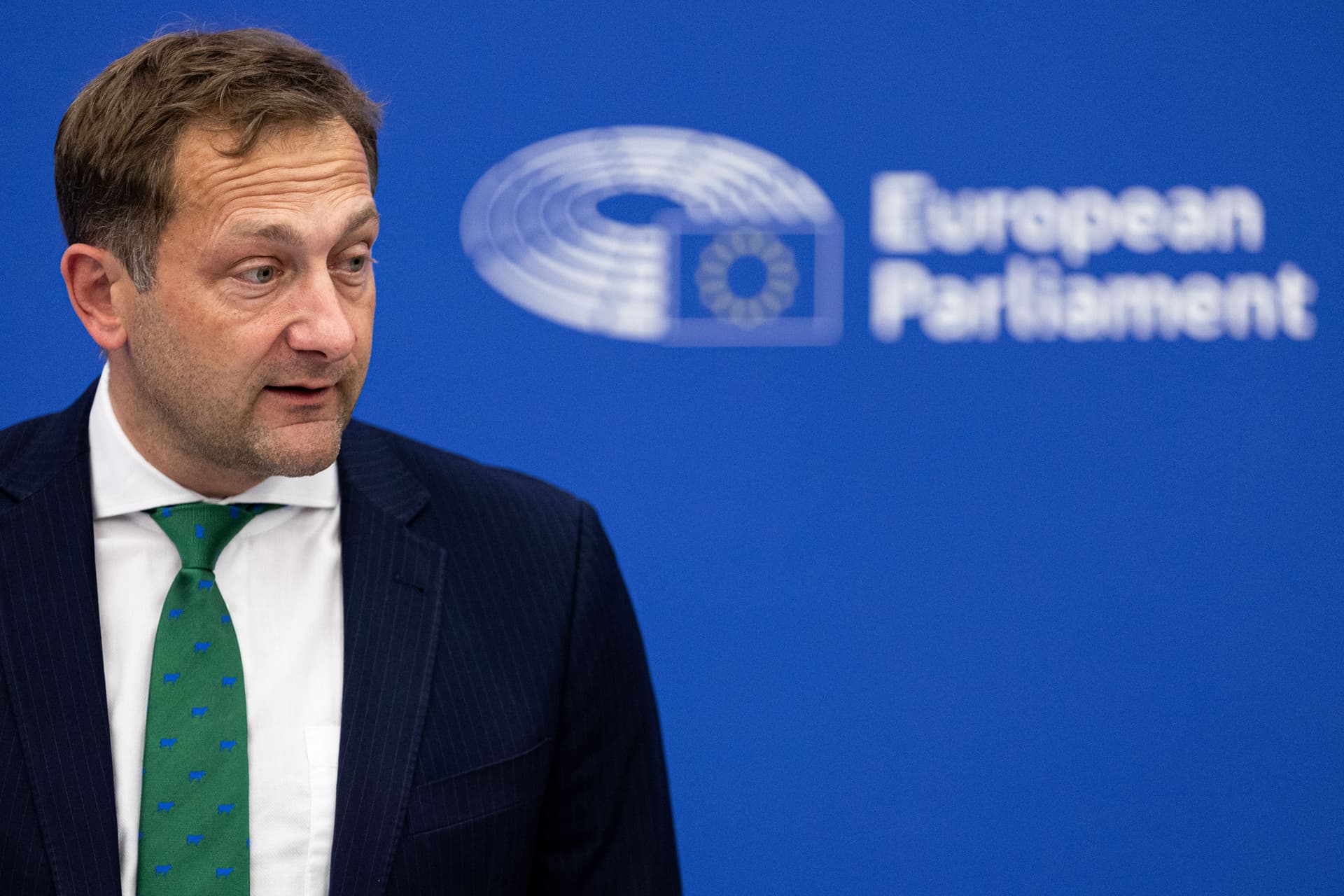 Landbrukskommissær Christophe Hansen står ved en talerstol i Strasbourg og presenterer EUs nye landbruksstrategi, med EU-flagg og en skjerm i bakgrunnen.