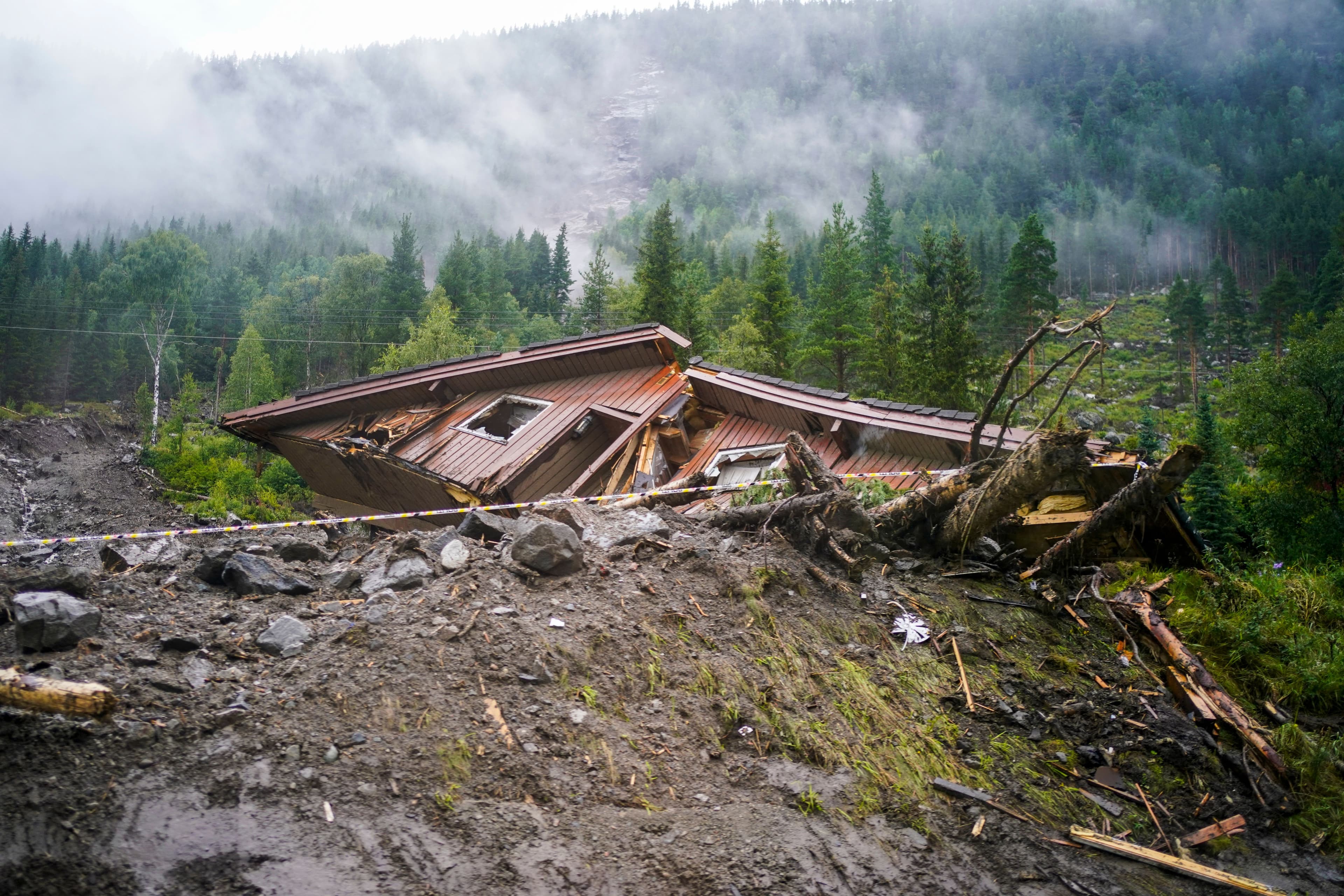 Ødelagt hus delvis begravd av et jordskred med gjørme, steiner og et veltet tre.