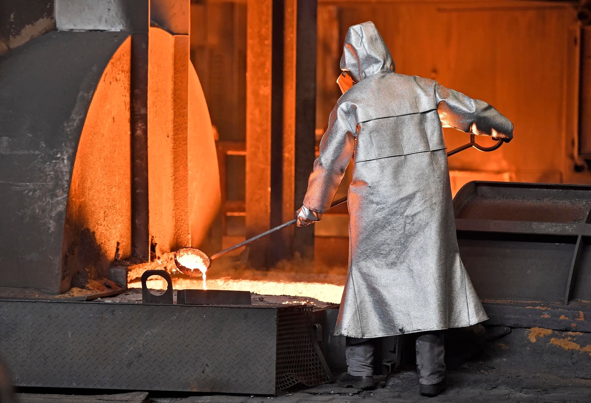 Støperiarbeider i refleksdrakt som heller smeltet metall.