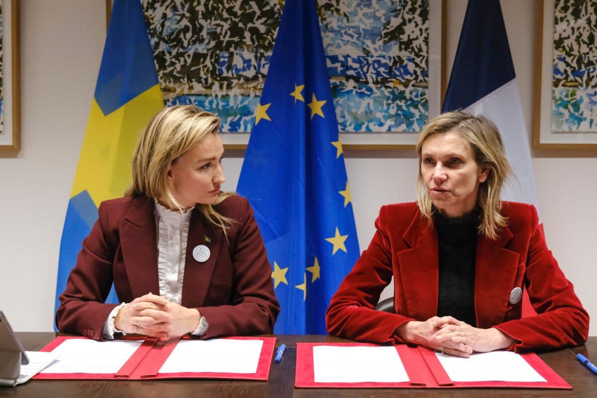 To kvinner sitter ved et bord foran flagg.