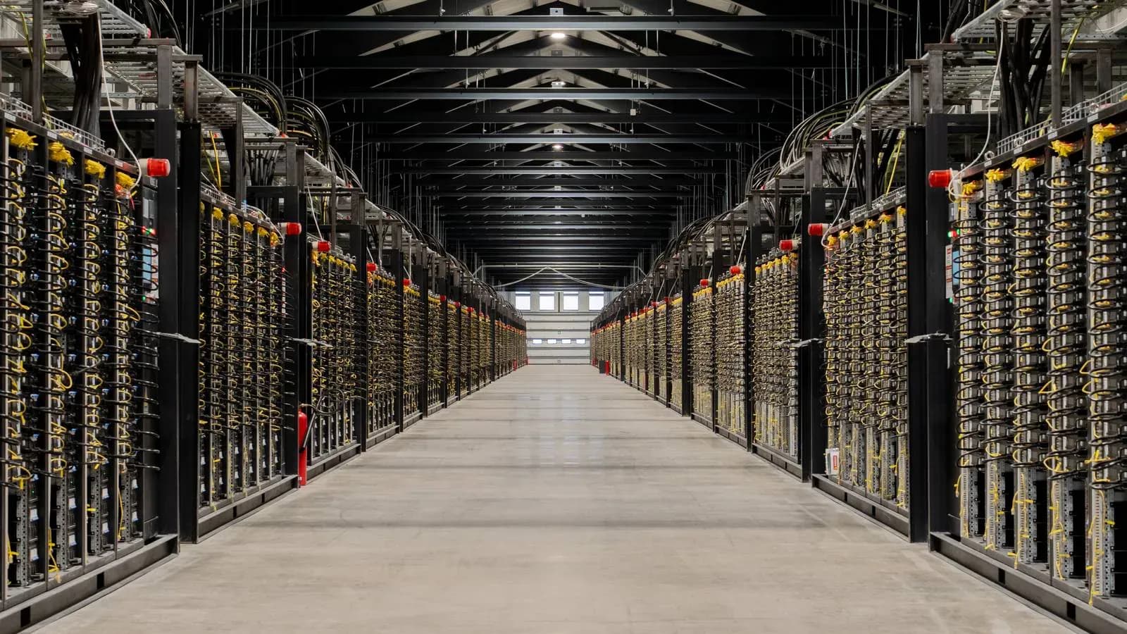 Lang midtgang i et stort datasenter, omgitt av serverrack fulle av gule kabler.