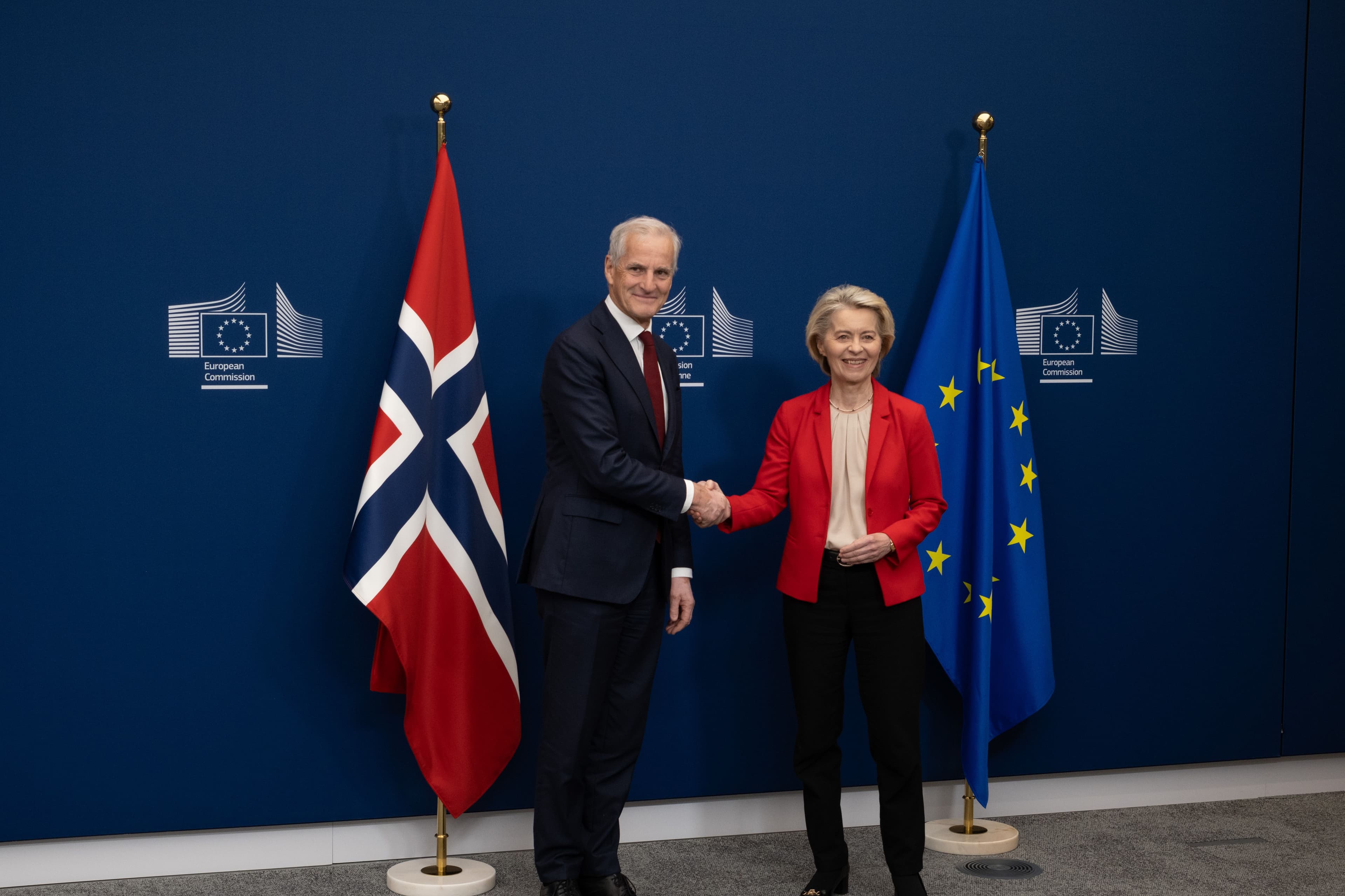 Jonas Gahr Støre tar Ursula von der Leyen i hånden, foran et norsk flagg og et EU flagg