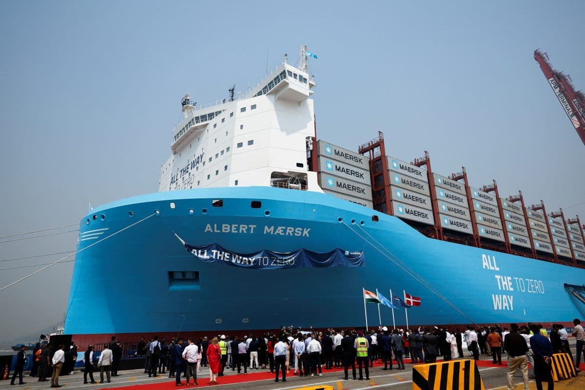 Et stort blått containerskip med «Albert Maersk» og «All the Way to Zero»-bannere ligger til kai ved en havn, omgitt av mennesker, med kraner i bakgrunnen.