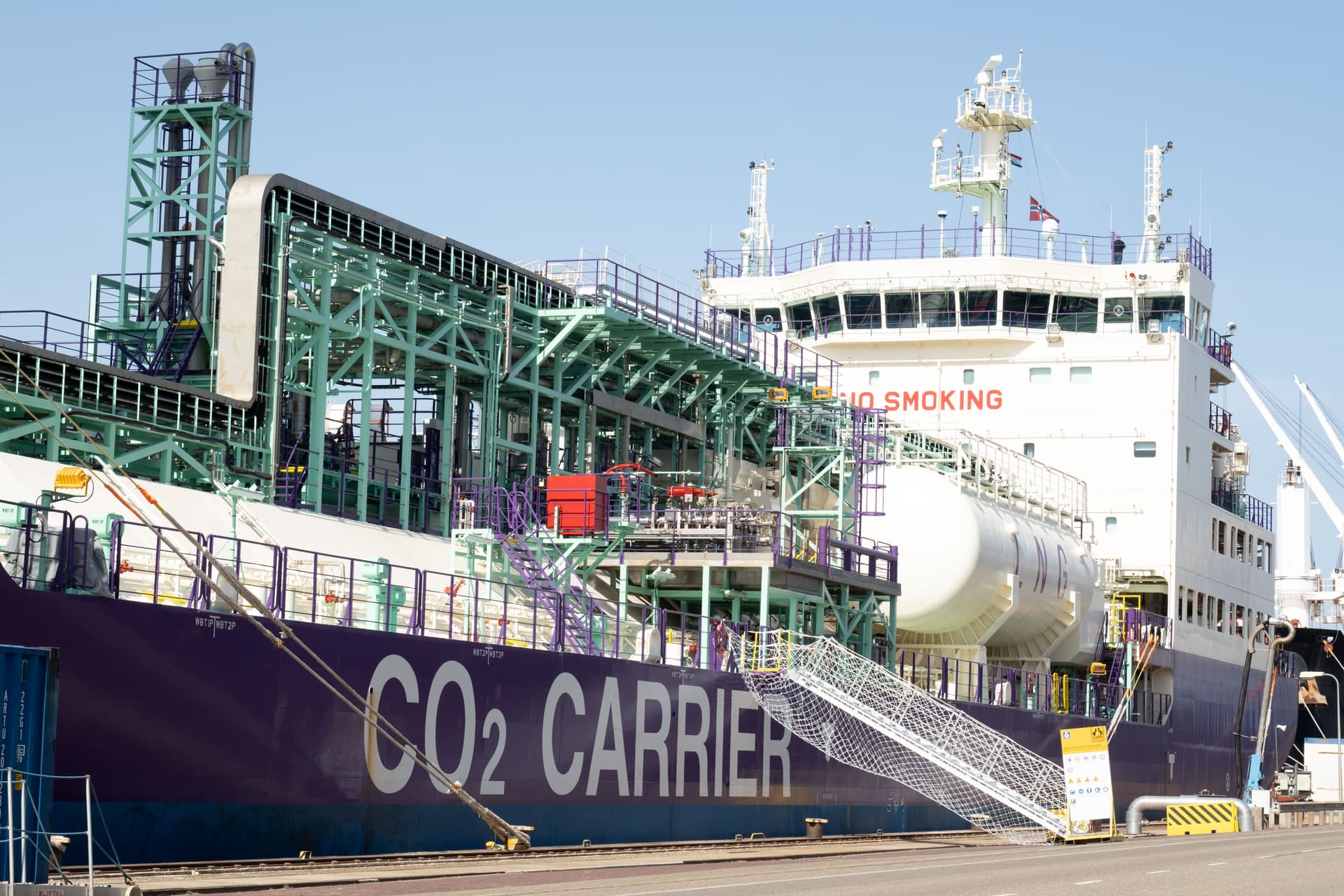 Et CO₂-transportskip ligger til kai i en havn, med industrielt utstyr og tanker synlig på dekk.