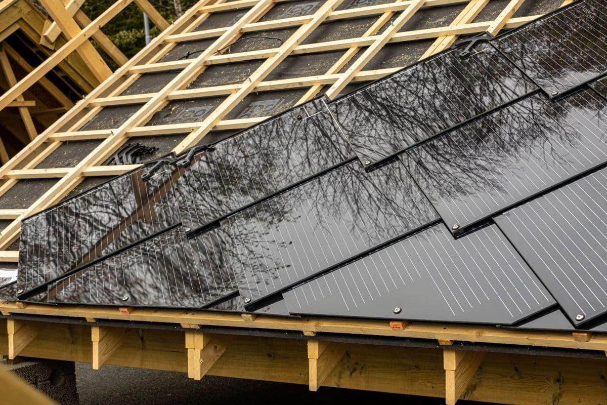 Nærbilde av et tak under konstruksjon med svarte soltakshingel delvis montert ved siden av eksponert treverk.