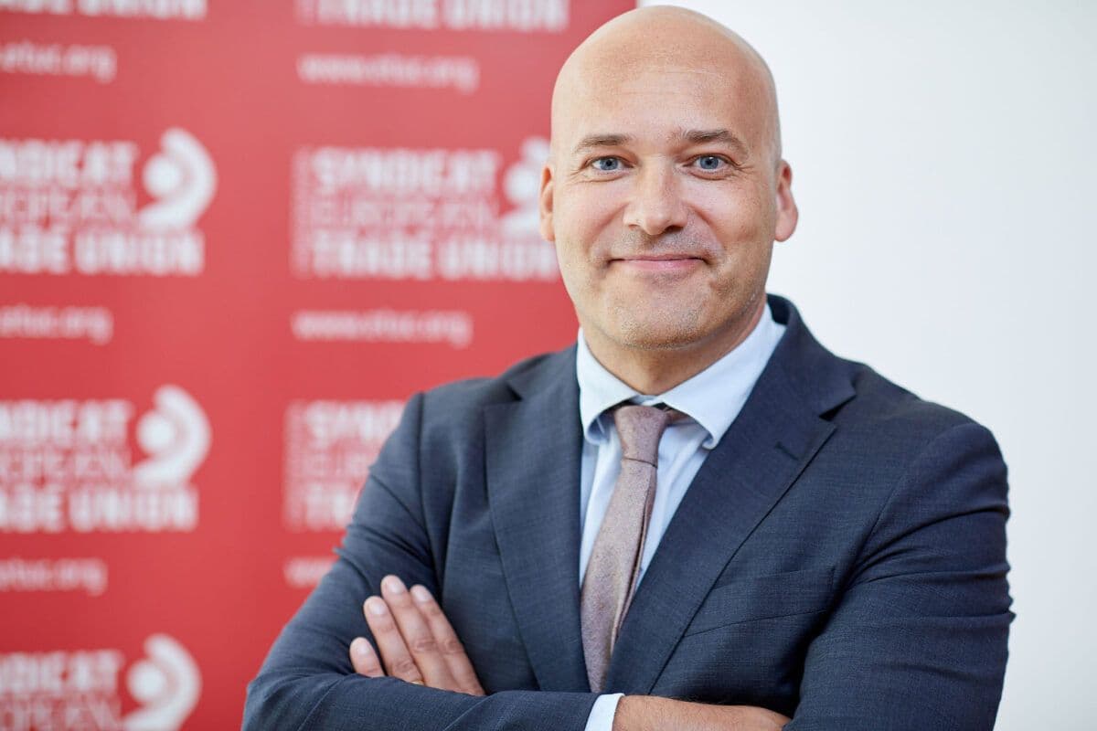 En mann i dress og slips som står foran en rød vegg.