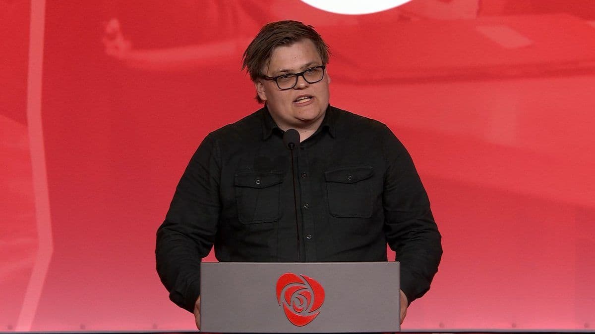 Person som snakker ved et podium med rød bakgrunn.