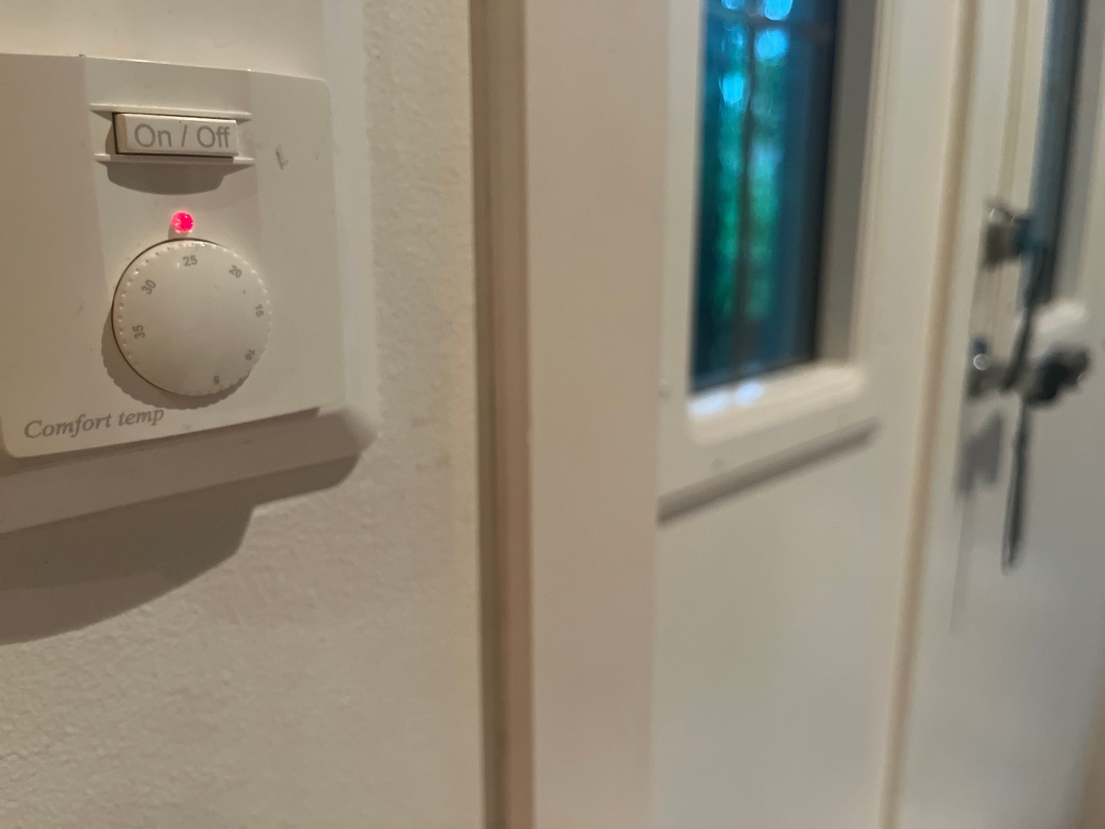En hvit veggmontert termostat med en av/på-bryter, en temperaturvelger og et rødt indikatorlys som lyser.