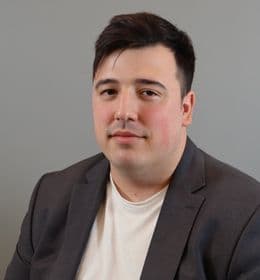 Mann med kort, mørkt hår iført grå dressjakke og hvit T-skjorte.