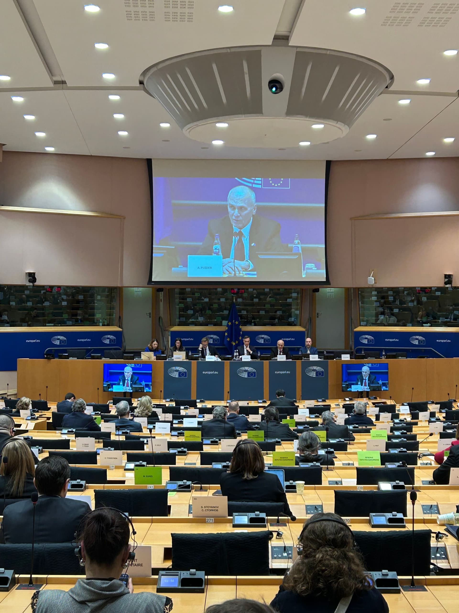 Publikum i Europaparlamentets plenumssal som ser på en taler på en stor skjerm.