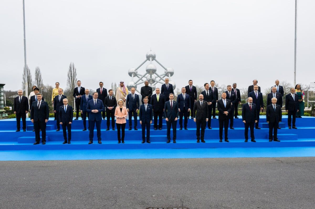 Gruppe av dignitærer poserer for et bilde på et offisielt arrangement med en metallisk skulptur i bakgrunnen.